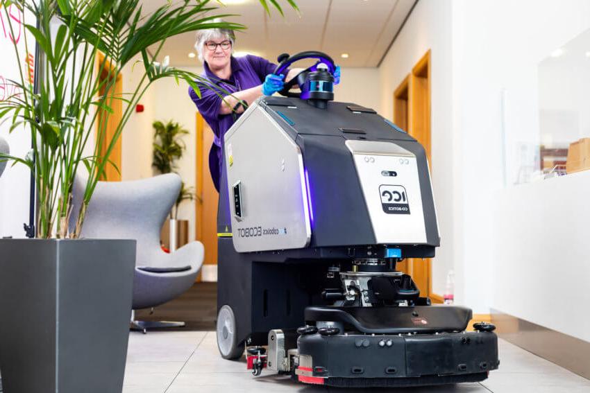 Mitie female cleaner turning the wheel on a robot floor cleaner in a corridor